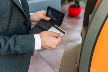 Cropped view of businessman putting credit card in wallet, while standing near atm with blurred street on background