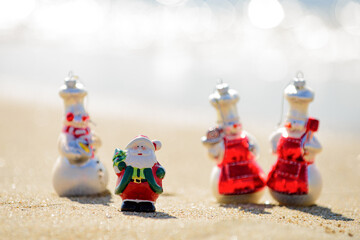 Positive sandy Snowman and Christmas Santa Claus at sunny tropical beach. New Year travel.