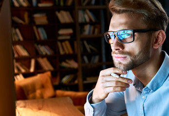 Serious focused businessman wearing computer glasses looking at pc screen with computer reflection using internet, watching webinar training, working online by video conference, close up face view.