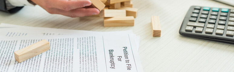 Cropped view of businessman with hand near block wood game falling near petition for bankruptcy at workplace, banner