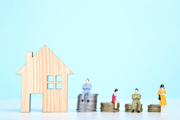 Wooden house model with miniature people and coins on blue background