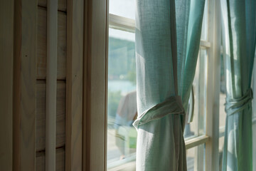 linen curtains of a soft turquoise color with a part of a white wooden window and a wall made of natural wood