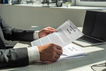 Cropped view of businessman holding petition for bankruptcy, while sitting at workplace on blurred background