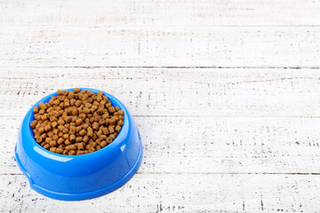 Dry pet food in bowl on white wooden table