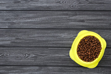 Dry pet food in bowl on black wooden table