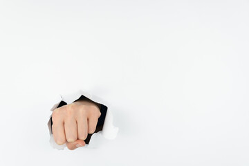 A woman's hand, clenched into a fist, pierces the white paper wall. The hand goes through the...