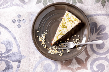 Piece of raw vegan cheesecake, no bake gluten free, decorated by lime zest and cashew nuts on plate on ornate ceramic table. Sunlight. Flat lay, space