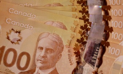 Canadian hundred dollar bills are scattered on a surface. 