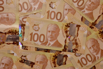 Canadian hundred dollar bills are scattered on a surface. 