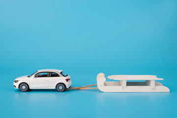 Christmas holidays concept. Close up photo of toy mini car carrying white wooden sledge isolated on blue background