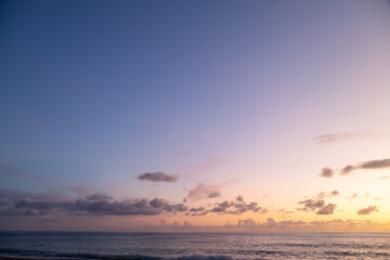 Dramatic sea shore sunset with sun setting down at the cloudy skyline with orange and vivid blues.