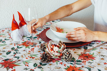 Christmas table decoration with floral tablecloth, decorative elements, glass of wine, white plates on a red trivet and aluminum cutlery. Christmas concept.