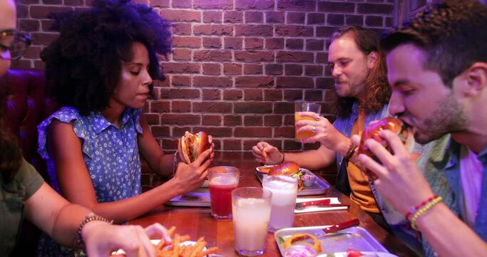 Group of friends drinking and eating burgers in retro restaurant