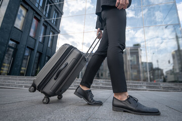 Close up picture of a man in a black suit carrying a suitcase