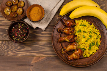 West African food. Rice with fried chicken and bananas, on a wooden background