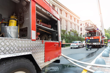 Firemen wearing uniform standing behind fire tape and many fire engine trucks with ladder at...