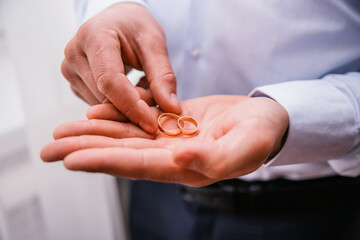 On a man's palm are two wedding rings. The groom holds the rings.