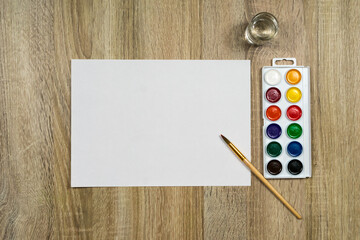 Watercolor paints and a brush with water on a wooden background. View from above. Place for an inscription.