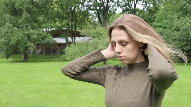 beautiful young blonde girl walks in a summer green park, posing, looking at the camera and straightens her hair full hd