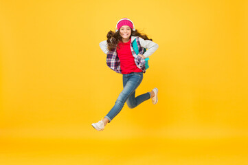 Fototapeta na wymiar Active small kid run with travel bag listening to music in headphones yellow background, traveling