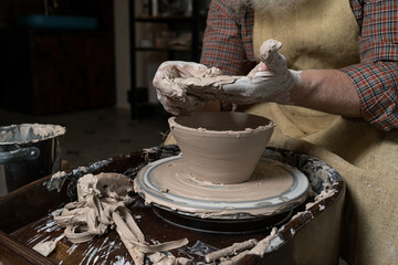 pottery, workshop, ceramics art concept - closeup on male hands sculpt new utensil with a tools and water, man's fingers work with potter wheel and raw fireclay, front close view
