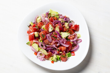 vegetable salad with  red onion, tomato, cucumber, avocado, dill, sumach, paprika, olive oil  in white bowl on wooden table