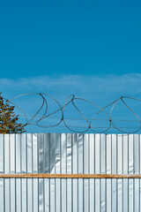 Barbed wire on a metal fence against a blue sky. Fence silt igda for