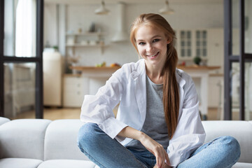 Portrait of happy redhead woman sitting on sofa at home, daydreaming.