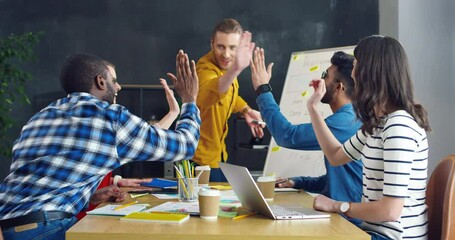 Happy cheerful multiethnic team of startuppers finishing their meeting and giving five to each other. Mixed-races students working together over new studying project. Managers at conference.