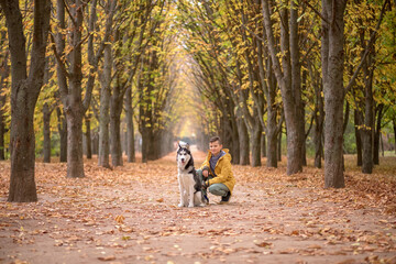 Fototapeta premium Handsome boy in a yellow raincoat with a husky dog in the fall forest