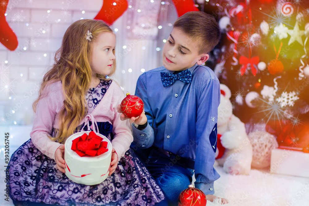 Wall mural children boy and girl sitting with large christmas balls on the background of the christmas tree . h