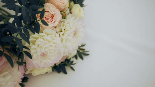 Three bouquets of flowers as a gift for the bridesmaids lie on a white tablecloth. The florist combined roses, peonies, chrysanthemums and ruscus branches in bouquets