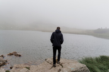 Men tourist is travelling and standing on the rocks near foggy lake. Hiking and climbing up to the top of the mountain. Tourism in Ukraine.