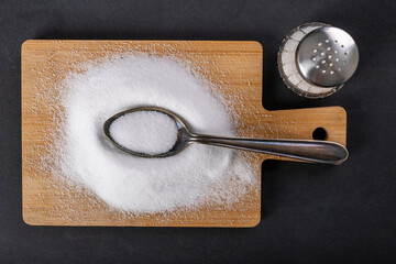 Metal spoon and spilled salt. A flavor enhancer added to dishes in home cooking.
