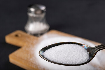Metal spoon and spilled salt. A flavor enhancer added to dishes in home cooking.