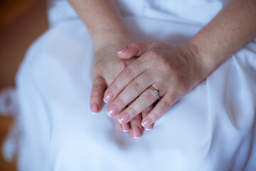 Young bride wearing beautiful engagement ring with diamond on white background. Close up of a brides hand on her lap. wedding ring on bride's finger