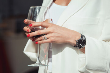 close-up of a hand of a senior woman with a glass of wine. Expensive exclusive watch, diamond rings, red nails