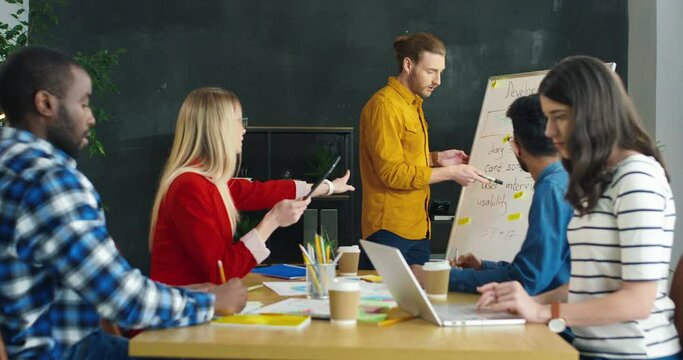 Mixed-races group of startuppers having meeting and discussing new project development in office. Caucasian man speak at conference of young multiethnic managers. Male reporting for colleagues.