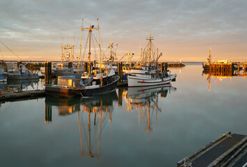 Fototapeta na wymiar Steveston Fishboats at Dawn. Calm water and clouds over the harbor of Steveston, British Columbia, Canada near Vancouver. Steveston is a small fishing village on the banks of the Fraser River.