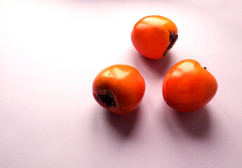 Three ripe persimmon fruits on a pastel background, close-up, side view, space for text