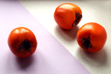 Three ripe persimmon fruits on a pastel and gray background, close-up, side view, space for text