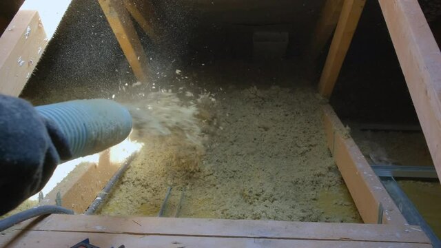Medium shot of thermal insulation of house with mineral wool in granules. Man making thermal roof insulation layer