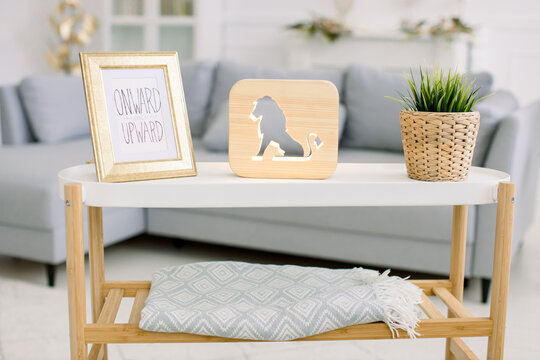 Home cozy decor and accessories. Coffee table with photo frame, decorative wooden lamp with lion picture, and artificial plant in wicker flower pot. Stylish interior of living room with gray sofa