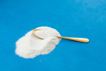 Pile collagen powder on blue textured background. Golden spoon and healthy food additive. Selective focus, copy space