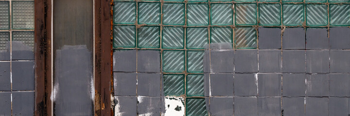 Old wall with a window made of square gray and glass tiles. Rough ribbed surface of dirty green glass. Vintage texture for background and design.