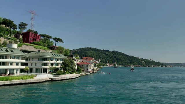 Footage of a yacht passing on Bosphorus, mansions at upscale neighborhood called "Kandilli" in Istanbul. It is a beautiful scene in a sunny summer day. Camera moves forward.