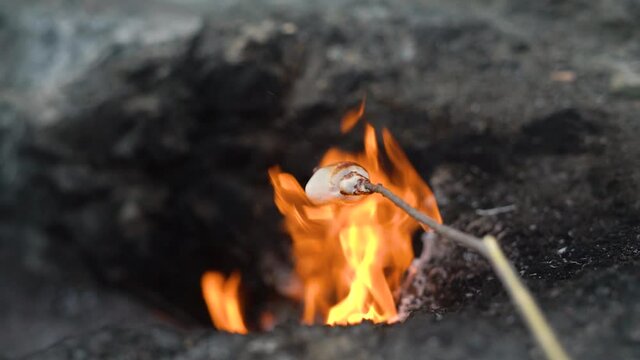 Long wooden stick with delicious marshmallow roasting over mystical Turkey landmark of bright flames burning on Chimaera mountain hillside close view.