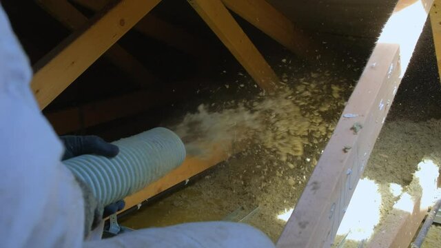 Thermal insulation of house with mineral wool in granules. Man making thermal roof insulation layer