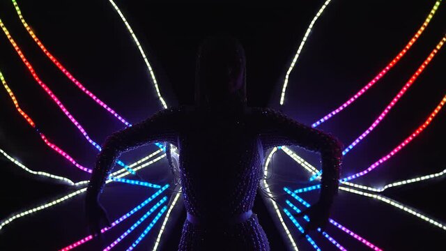 A young woman in the image of a butterfly with glowing and flashing wings poses against the background of dynamic spotlights. Silhouette. Close up.