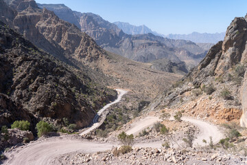 A steep mountain road winds through the rugged terrain of Oman on 7 February 2020, its sharp hairpin bends descending from rocky cliffs into a remote canyon landscape under a clear blue sky.
